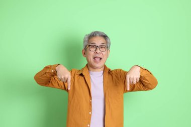 40 'lı yaşlarda yeşil arka planda duran sarı gömlekli Asyalı bir adam..