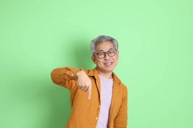 40 'lı yaşlarda yeşil arka planda duran sarı gömlekli Asyalı bir adam..