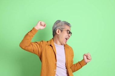 40 'lı yaşlarda yeşil arka planda duran sarı gömlekli Asyalı bir adam..