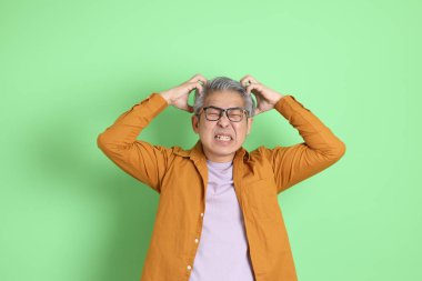 40 'lı yaşlarda yeşil arka planda duran sarı gömlekli Asyalı bir adam..