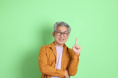 40 'lı yaşlarda yeşil arka planda duran sarı gömlekli Asyalı bir adam..