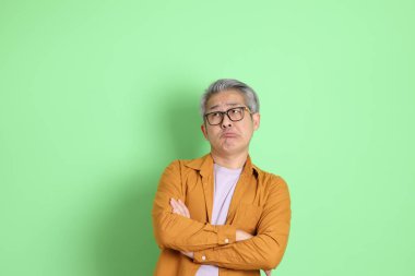 40 'lı yaşlarda yeşil arka planda duran sarı gömlekli Asyalı bir adam..