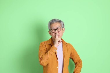 40 'lı yaşlarda yeşil arka planda duran sarı gömlekli Asyalı bir adam..