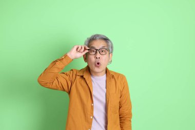 40 'lı yaşlarda yeşil arka planda duran sarı gömlekli Asyalı bir adam..