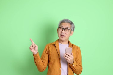 40 'lı yaşlarda yeşil arka planda duran sarı gömlekli Asyalı bir adam..