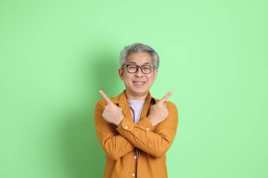 40 'lı yaşlarda yeşil arka planda duran sarı gömlekli Asyalı bir adam..