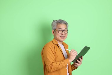 40 'lı yaşlarda yeşil arka planda duran sarı gömlekli Asyalı bir adam..