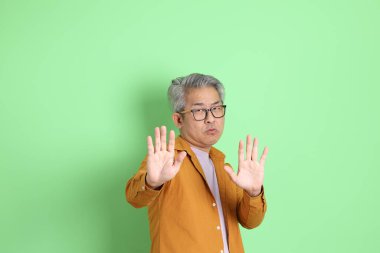 40 'lı yaşlarda yeşil arka planda duran sarı gömlekli Asyalı bir adam..