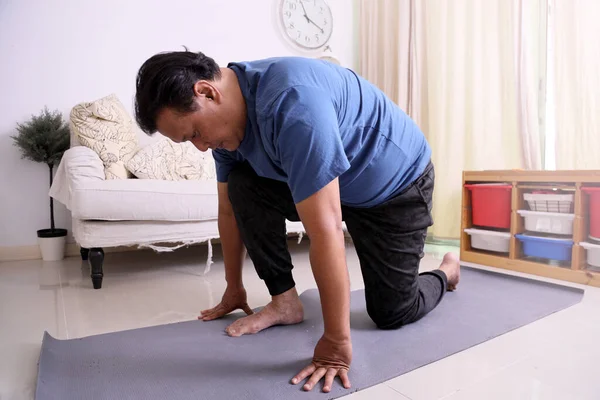 40多岁的亚洲成年超重男子在电视上看体育节目 并在客厅的地图上做瑜伽 — 图库照片