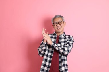 40 'lı yaşlarda Asyalı bir adam pembe arka planda sıradan kıyafetlerle dolanıyor..