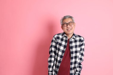 40 'lı yaşlarda Asyalı bir adam pembe arka planda sıradan kıyafetlerle dolanıyor..