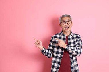 40 'lı yaşlarda Asyalı bir adam pembe arka planda sıradan kıyafetlerle dolanıyor..