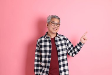 40 'lı yaşlarda Asyalı bir adam pembe arka planda sıradan kıyafetlerle dolanıyor..