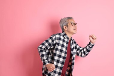 40 'lı yaşlarda Asyalı bir adam pembe arka planda sıradan kıyafetlerle dolanıyor..