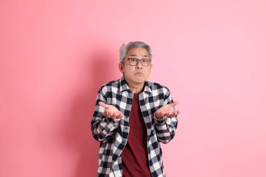 40 'lı yaşlarda Asyalı bir adam pembe arka planda sıradan kıyafetlerle dolanıyor..