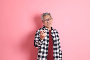 40 'lı yaşlarda Asyalı bir adam pembe arka planda sıradan kıyafetlerle dolanıyor..