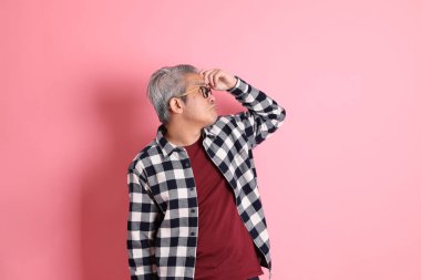 40 'lı yaşlarda Asyalı bir adam pembe arka planda sıradan kıyafetlerle dolanıyor..