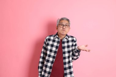 40 'lı yaşlarda Asyalı bir adam pembe arka planda sıradan kıyafetlerle dolanıyor..