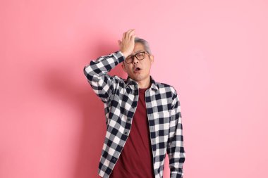 40 'lı yaşlarda Asyalı bir adam pembe arka planda sıradan kıyafetlerle dolanıyor..