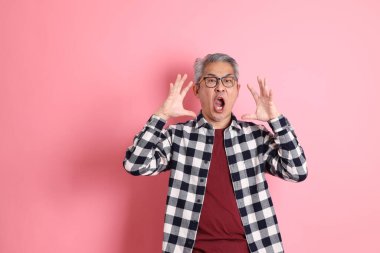 40 'lı yaşlarda Asyalı bir adam pembe arka planda sıradan kıyafetlerle dolanıyor..