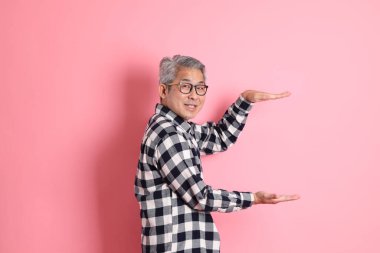 40 'lı yaşlarda Asyalı bir adam pembe arka planda sıradan kıyafetlerle dolanıyor..