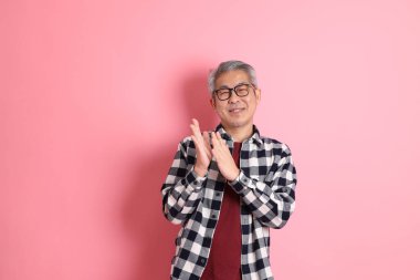 40 'lı yaşlarda Asyalı bir adam pembe arka planda sıradan kıyafetlerle dolanıyor..