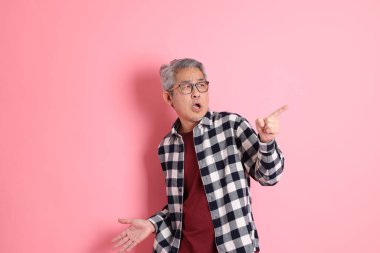 40 'lı yaşlarda Asyalı bir adam pembe arka planda sıradan kıyafetlerle dolanıyor..