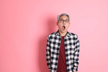 40 'lı yaşlarda Asyalı bir adam pembe arka planda sıradan kıyafetlerle dolanıyor..