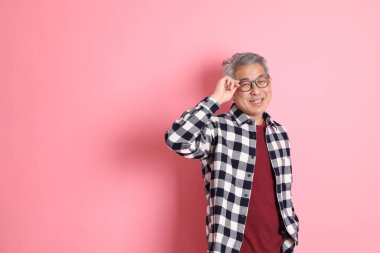 40 'lı yaşlarda Asyalı bir adam pembe arka planda sıradan kıyafetlerle dolanıyor..