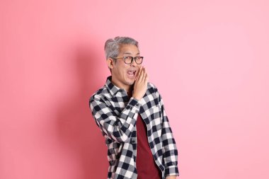 40 'lı yaşlarda Asyalı bir adam pembe arka planda sıradan kıyafetlerle dolanıyor..