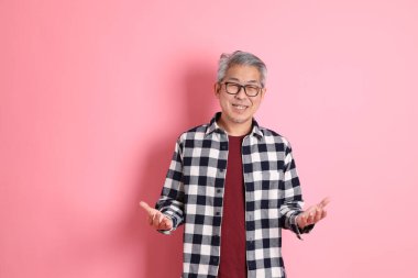 40 'lı yaşlarda Asyalı bir adam pembe arka planda sıradan kıyafetlerle dolanıyor..