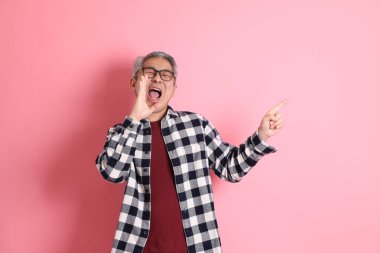 40 'lı yaşlarda Asyalı bir adam pembe arka planda sıradan kıyafetlerle dolanıyor..