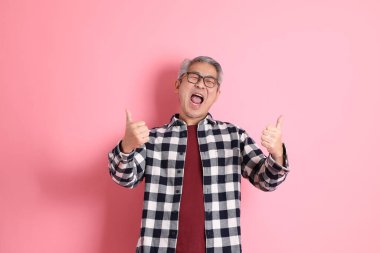 40 'lı yaşlarda Asyalı bir adam pembe arka planda sıradan kıyafetlerle dolanıyor..