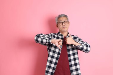 40 'lı yaşlarda Asyalı bir adam pembe arka planda sıradan kıyafetlerle dolanıyor..