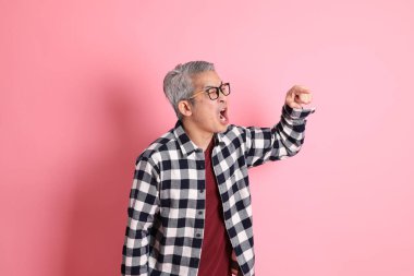 40 'lı yaşlarda Asyalı bir adam pembe arka planda sıradan kıyafetlerle dolanıyor..