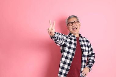 40 'lı yaşlarda Asyalı bir adam pembe arka planda sıradan kıyafetlerle dolanıyor..