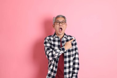 40 'lı yaşlarda Asyalı bir adam pembe arka planda sıradan kıyafetlerle dolanıyor..