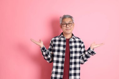 40 'lı yaşlarda Asyalı bir adam pembe arka planda sıradan kıyafetlerle dolanıyor..