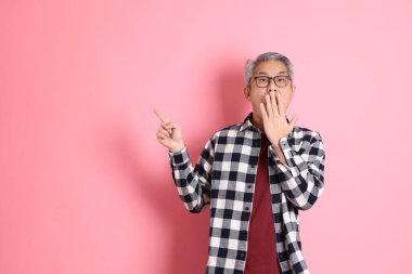 40 'lı yaşlarda Asyalı bir adam pembe arka planda sıradan kıyafetlerle dolanıyor..