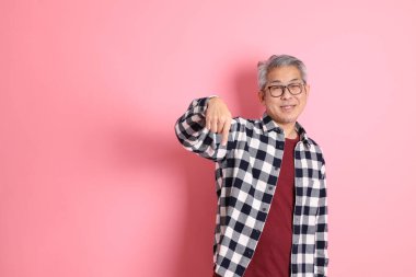 40 'lı yaşlarda Asyalı bir adam pembe arka planda sıradan kıyafetlerle dolanıyor..