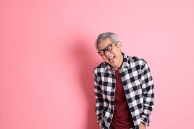 40 'lı yaşlarda Asyalı bir adam pembe arka planda sıradan kıyafetlerle dolanıyor..