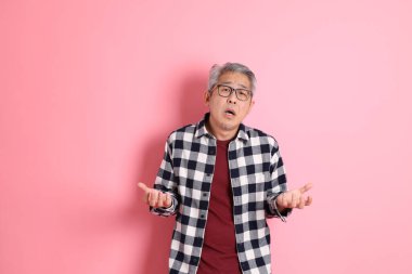 40 'lı yaşlarda Asyalı bir adam pembe arka planda sıradan kıyafetlerle dolanıyor..