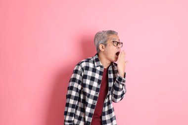 40 'lı yaşlarda Asyalı bir adam pembe arka planda sıradan kıyafetlerle dolanıyor..