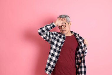 40 'lı yaşlarda Asyalı bir adam pembe arka planda sıradan kıyafetlerle dolanıyor..