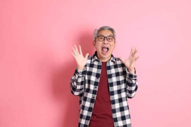 40 'lı yaşlarda Asyalı bir adam pembe arka planda sıradan kıyafetlerle dolanıyor..