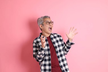 40 'lı yaşlarda Asyalı bir adam pembe arka planda sıradan kıyafetlerle dolanıyor..