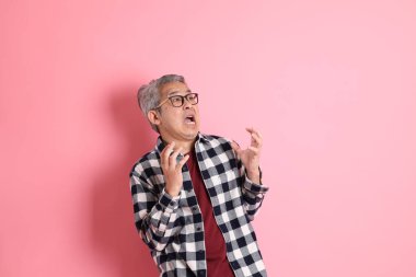 40 'lı yaşlarda Asyalı bir adam pembe arka planda sıradan kıyafetlerle dolanıyor..