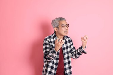 40 'lı yaşlarda Asyalı bir adam pembe arka planda sıradan kıyafetlerle dolanıyor..