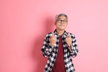 40 'lı yaşlarda Asyalı bir adam pembe arka planda sıradan kıyafetlerle dolanıyor..