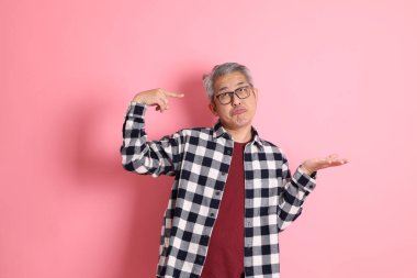 40 'lı yaşlarda Asyalı bir adam pembe arka planda sıradan kıyafetlerle dolanıyor..